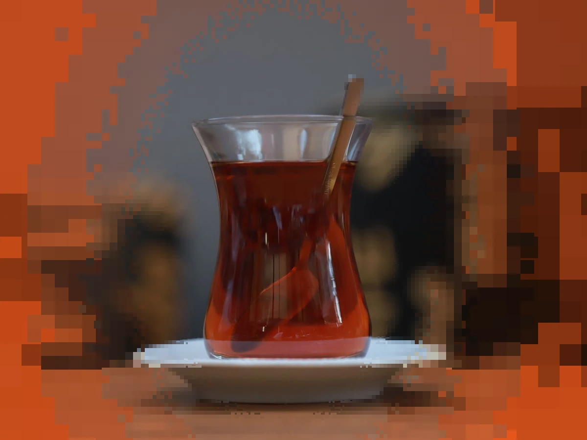 A tulip shaped glass of dark red tea with a spoon on a white saucer, sharp in the middle and breaking into warm pixels at the edges